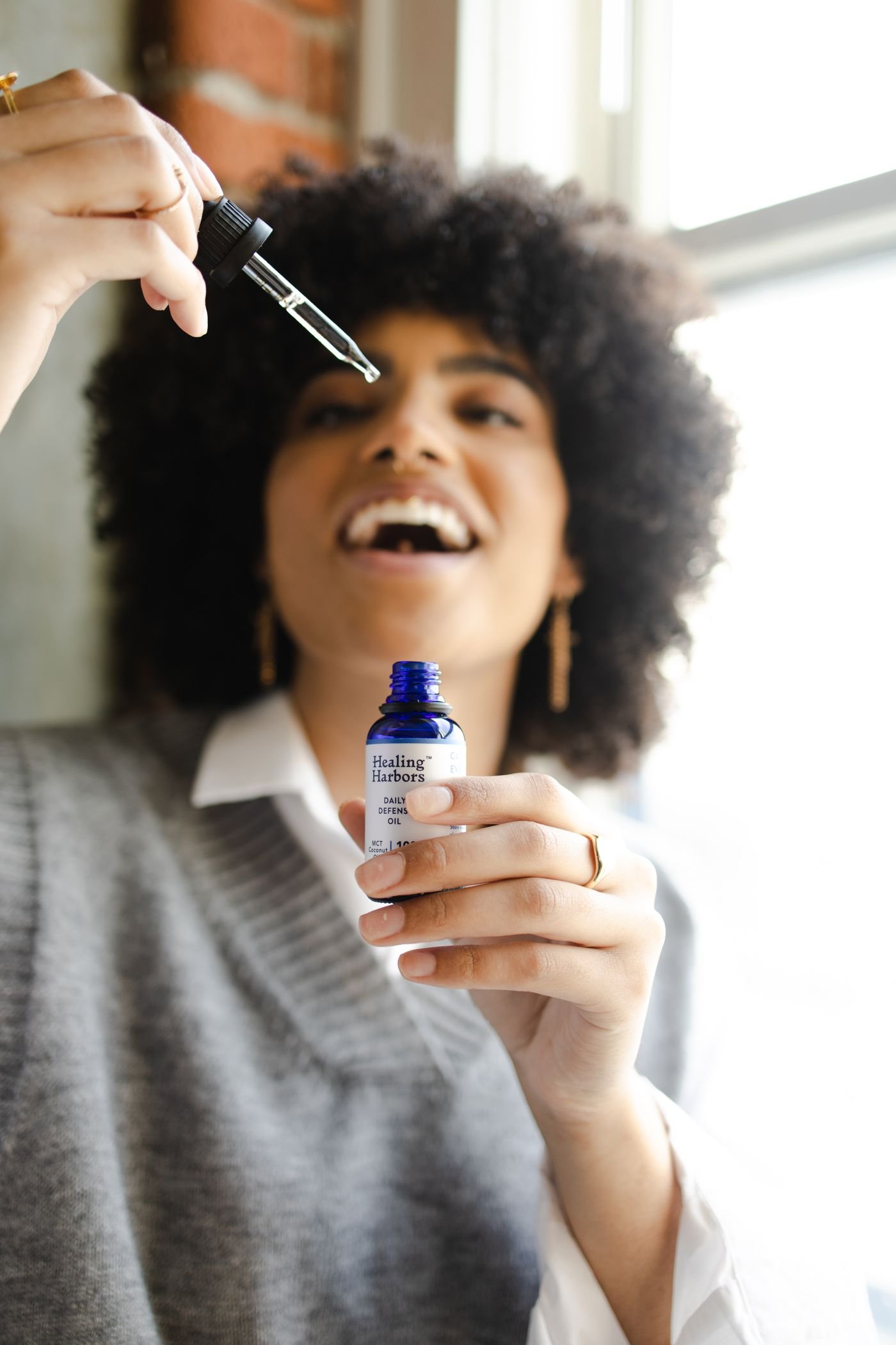 Woman laughing while holding a serum dropper in bright daylight
