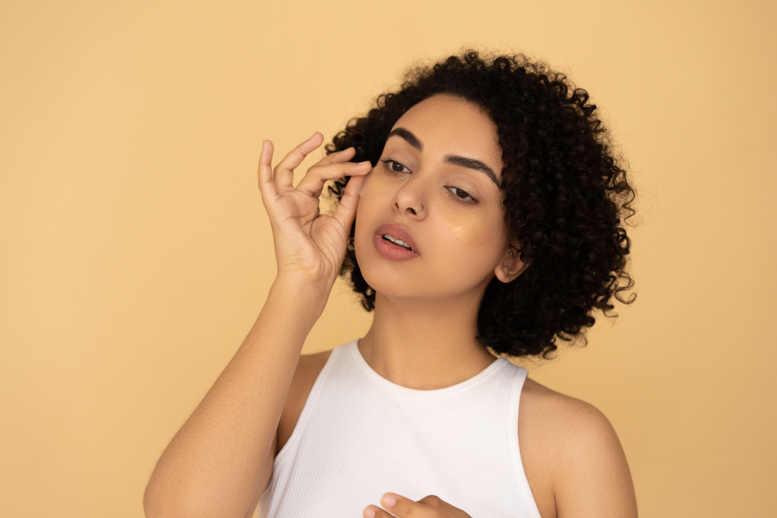 Woman with curly hair applying an under-eye patch