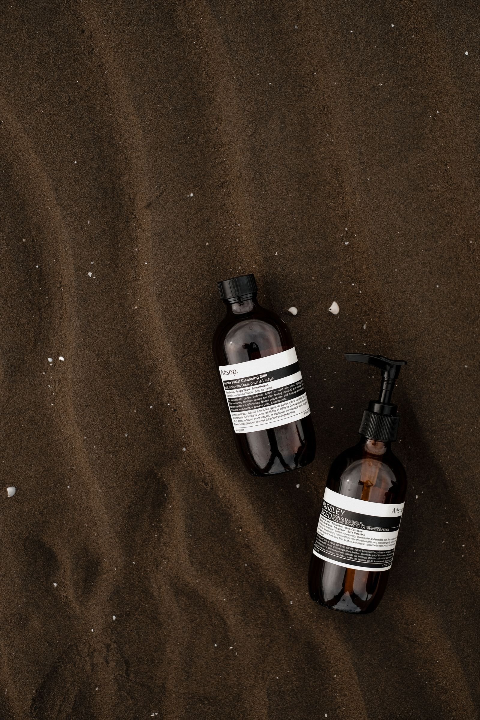 Two minimalist cosmetic bottles on rippled dark sand