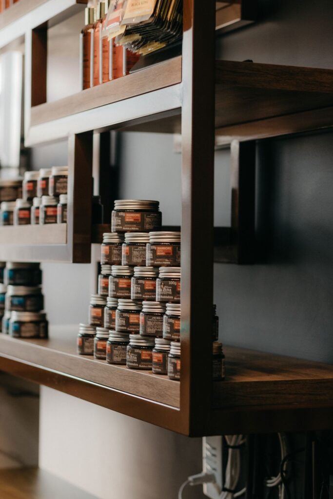 Glass jars of hair and skin cream lined up on warm wooden shop shelves