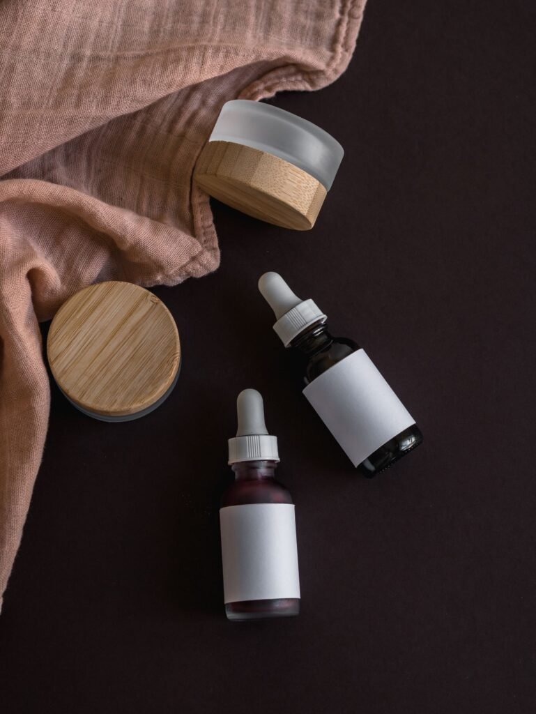 A glass dropper bottle and a wooden-lidded jar of serum on a dark surface