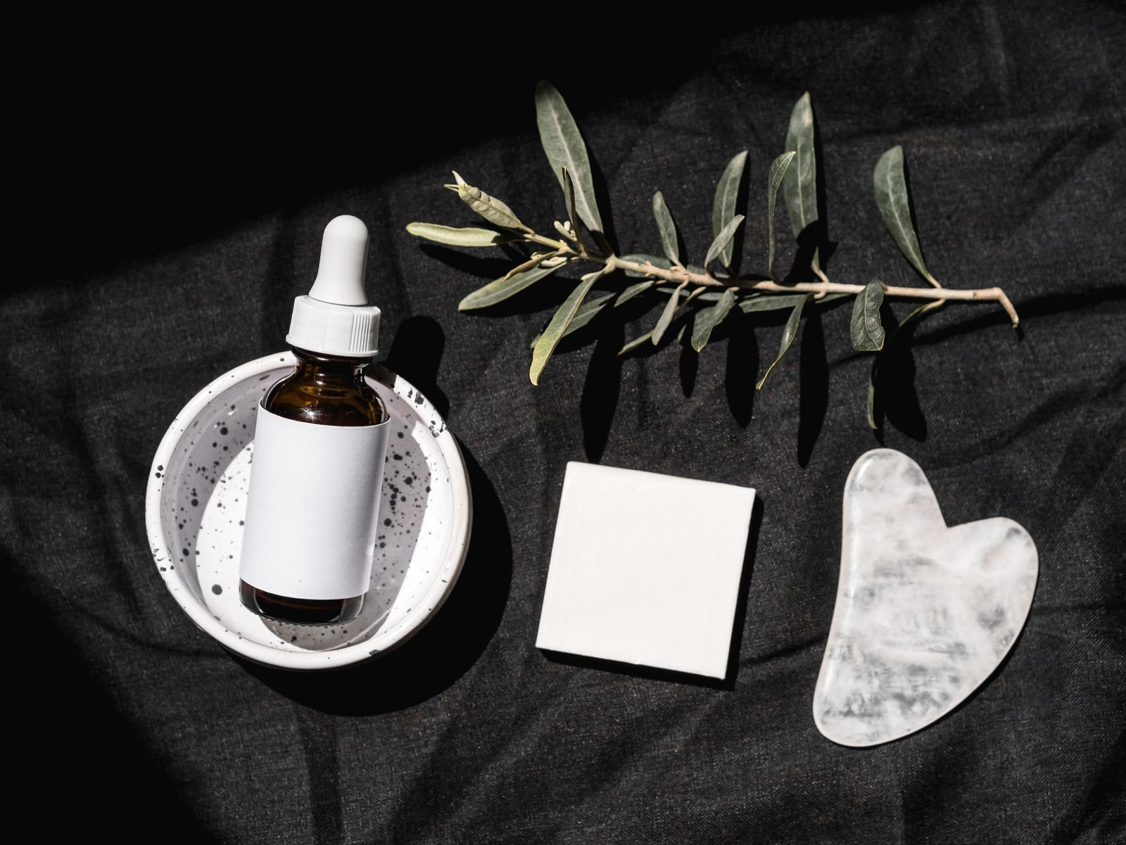 A serum dropper bottle and a gua sha stone arranged on a pale background