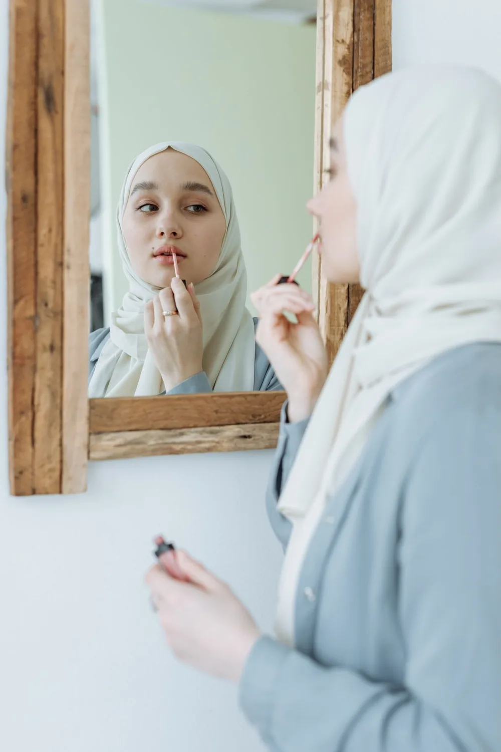 Woman in a hijab applying lip gloss in a mirror